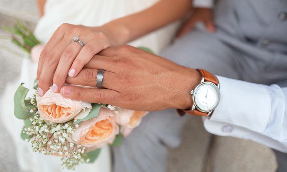 Hands with wedding rings over a bouquet of roses.